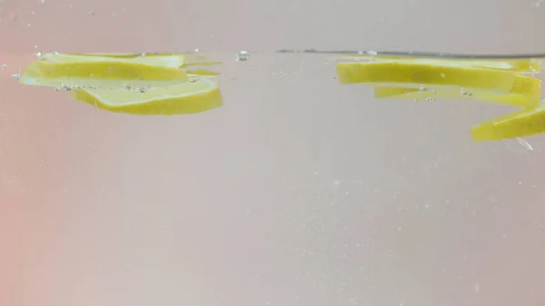 Крупный план падения ломтиков лимона в брызги воды. Начали. Свежие цитрусовые фруктовые ломтики падают в свежий витаминный напиток. — стоковое фото