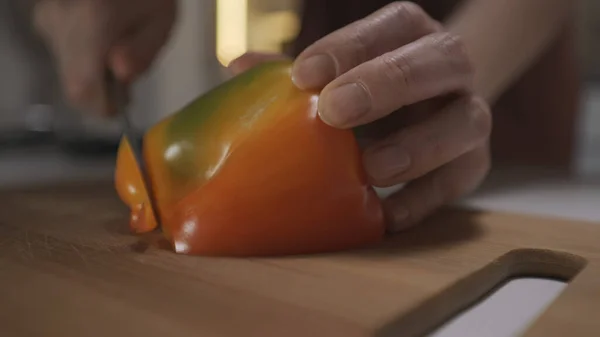 Fermer les mains de la femme à l'aide d'un couteau de cuisine pour trancher et couper le poivron sur une planche de bois. L'action. Concept de régime végétal sain et cuisson des aliments. — Photo