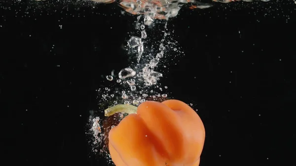 Friss piros édes paprika esik a vízbe légbuborékok. Felvétel. Zárja le a lassított felvétel ízletes zöldség dobott egy víz teli tartály fekete háttér. — Stock Fotó
