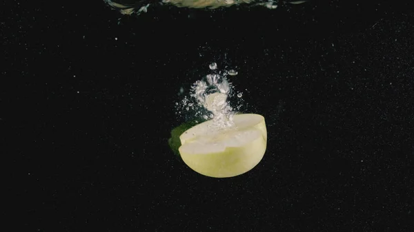 Közel egy alma félig dobott a vízbe elszigetelt fekete háttér. Felvétel. Zöld alma átlátszó vízben, légbuborékokkal, vitaminokkal és egészséges étrenddel. — Stock Fotó