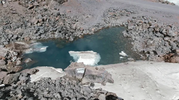 Eine Wasserpfütze auf einem Bergfelsen. Clip. Sonniger Berghang mit einer Pfütze aus dunkelblauem Wasser, umgeben von großen und kleinen Steinen. — Stockfoto