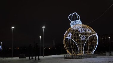 Gece açık havada güzel bir yeni yıl heykelinin çelenklerle süslenmiş bir top oyuncağı şeklinde görüntüsü. Kavram. Şehir sokak dekorasyonu. Yuvarlak şekilli oyuncak topu figürü. Noel temalı..