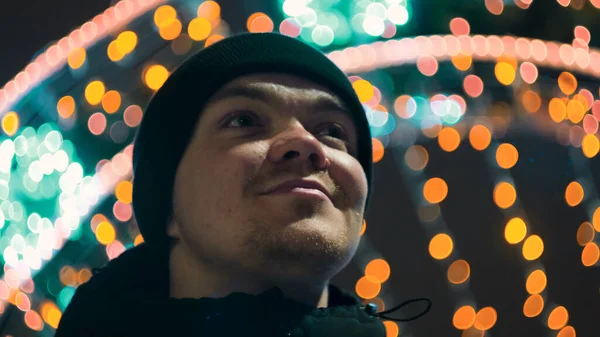 A fiatalember a karácsonyi város fényeit nézi. Fogantatás. A mosolygós fiatalember a város gyönyörű karácsonyi dekorációit nézi. Az ember úgy néz ki, csodálattal karácsonyi dekorációk a háttérben — Stock Fotó