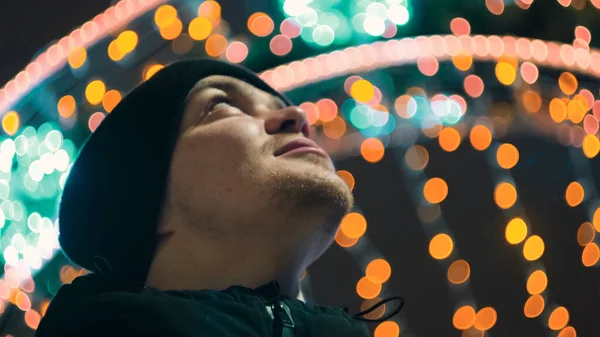 Nuori mies katsoo joulukaupungin valoja. Konsepti. Nuori mies, jolla on hymy, katsoo kauniita kaupungin joulukoristeita. Mies näyttää ihaillen joulukoristeet taustalla — kuvapankkivalokuva
