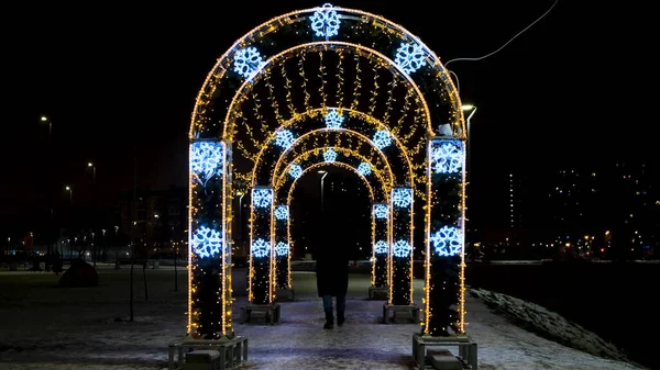 Arches decorated with garlands in city park. Concept. People pass through arches with garlands. People walk under arches decorated with garlands glowing brightly in evening — Stock Photo, Image