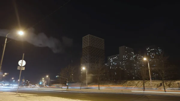 Time lapse of the winter night road in the city sleeping area. Action. Dark city landscape with a smoking chimney and residential houses.