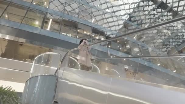 Frau in beigem Mantel und schwarzem Hut auf der Rolltreppe im modernen Einkaufszentrum. Handeln. Junge Frau hält eine professionelle Kamera in der Hand und fotografiert in einem Einkaufszentrum. — Stockvideo