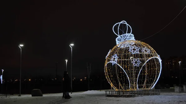 Night outdoors view of a beautiful New Year sculpture in a form of ball toy decorated by garlands. Concept. City street decoration with illuminated figure of round shaped toy ball, Christmas theme. — Stock Photo, Image