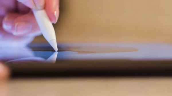 Close up de uma jovem mulher usando um tablet para o trabalho, freelance. Conceito. Mão feminina tocando a tela de uma almofada digital e tomando um estilete branco. — Fotografia de Stock