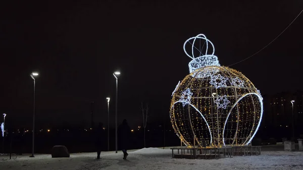 Night outdoors view of a beautiful New Year sculpture in a form of ball toy decorated by garlands. Concept. City street decoration with illuminated figure of round shaped toy ball, Christmas theme. — Stock Photo, Image