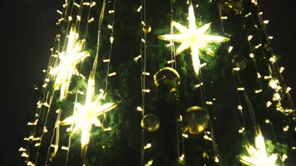 Close up de árvore de Natal decorado por guirlandas douradas e estrelas ao ar livre à noite. Conceito. Árvore de abeto de Ano Novo iluminada na rua de cidade. — Fotografia de Stock