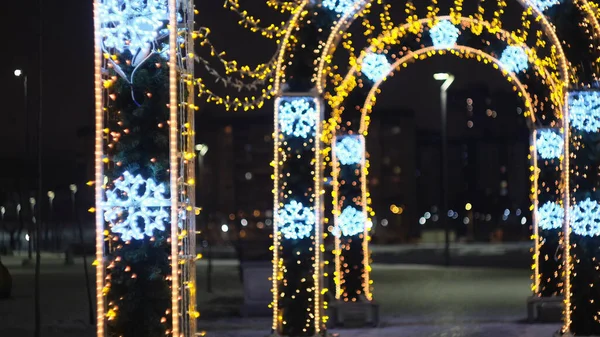Novoroční osvětlení s řadou oblouků zdobených zlatými věnci a modrými sněhovými vločkami. Koncept. Vánoční ozdoby ve městě ulice pozdě večer. — Stock fotografie