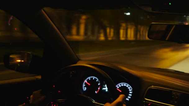 Θέα από το εσωτερικό του αυτοκινήτου του ανθρώπου χέρια οδήγηση ενός οχήματος τη νύχτα. Στικ. Κινούμενοι κατά μήκος κτιρίων, δέντρων και άδειων σκοτεινών δρόμων κάτω από κίτρινα φανάρια. — Αρχείο Βίντεο