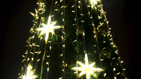 La decoración de la ciudad el árbol de navidad de fiesta. Concepto. Vista inferior de un abeto verde de Año Nuevo iluminado por las guirnaldas doradas y los copos de nieve artificiales brillantes sobre el fondo del cielo negro. —  Fotos de Stock