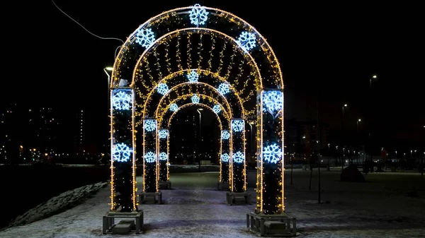 Bożonarodzeniowe iluminacje i dekoracje na ulicy miejskiej w formie łuków. Koncepcja. Piękne światła jako symbol ferii zimowych, błyszcząca girlanda na czarnym tle nieba. — Zdjęcie stockowe