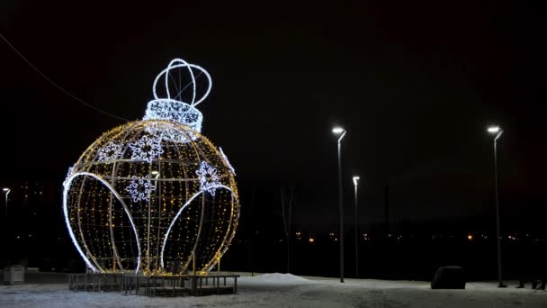 Nattutsikt över två silhuetter promenader runt en underbar jätte leksak bollen figur dekorerad med lysande led ljus. Begreppet. Nattvinter park med lyktor och juldekorationer. — Stockvideo