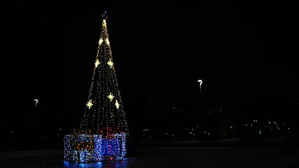 Osamělý vánoční stromek v prázdné městské ulici v noci. Koncept. City park s vyzdobenou krásnou smrk strom s girlandy a dvě současné krabice na černém pozadí oblohy. — Stock fotografie
