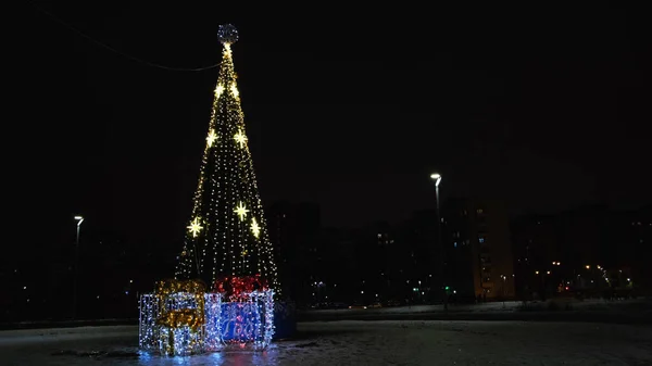 Arbre de Noël solitaire dans la rue vide de la ville la nuit. Concept. Parc municipal avec beau sapin décoré avec des guirlandes et deux boîtes cadeaux sur fond de ciel noir. — Photo