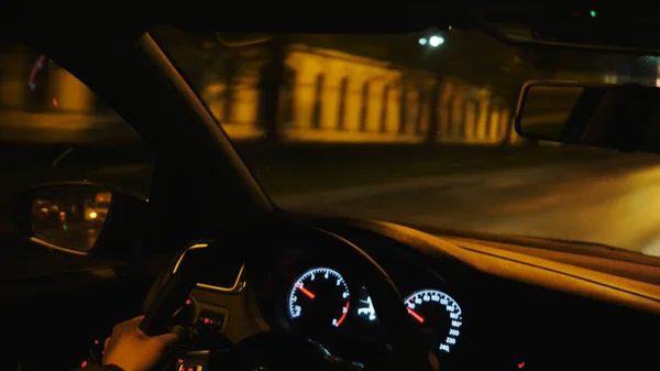 View from inside the car of man hands driving a vehicle at night. Stock footage. Moving along buildings, trees, and empty dark streets under yellow lanterns light.