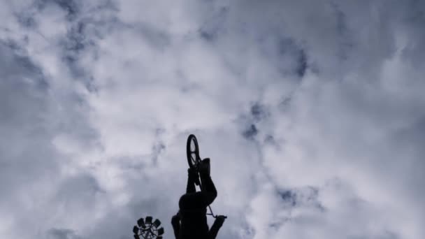 Nederst ser man en gutt med silhuett som hopper med sin bmx-sykkel på blå, skyet bakgrunn. Handling. Utføre et triks med dødt sløyfe, konseptet om ekstremsport. – stockvideo