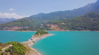 Dağlardaki turkuaz göl manzaralı güzel bir pelerin. Şarjör. Turkuaz gölün ortasına kadar uzanıyor. Güneşli yaz gününde dağlarla çevrili turkuaz gölde güzel bir pelerin.