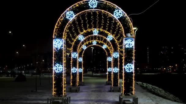 Illuminazioni di Natale e decorazioni nella strada di città in una forma di archi. Concetto. Belle luci come simbolo di vacanze invernali, ghirlanda splendente su sfondo cielo nero. — Video Stock