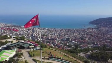 Arka planda güzel bir deniz manzarası olan Türk Bayrağının rüzgarda dalgalanmasını gösteren hava manzarası. Şarjör. Sahil şehri ve sonsuz denizi olan güzel bir manzara.. 