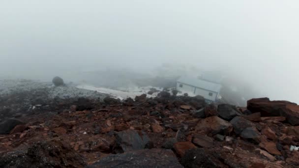Piccolo rifugio per arrampicatori situato in montagna in una giornata nebbiosa e nuvolosa, effetto timelapse. Clip. Rifugio per alpinisti, casette su un pendio roccioso. — Video Stock
