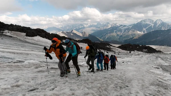 Os viajantes sobem ao longo do passo da montanha na encosta do gelo. Clipe. Conceito de esporte extremo e hobbies, alpinistas no fundo da cordilheira e nuvens pesadas. — Fotografia de Stock