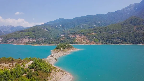 Top uitzicht op prachtige kaap in turquoise meer in de bergen. Een knip. Lange kaap strekt zich uit tot midden in het turquoise meer. Prachtige kaap in turquoise meer omgeven door bergen op zonnige zomerdag — Stockfoto