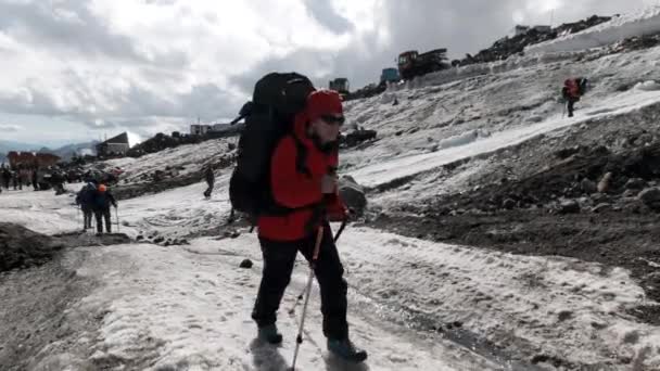 Montañeros subiendo una colina a lo largo de una ladera nevada cerca de la base del campamento. Clip. Alpes Occidentales, Europa explorando el mundo a través del estilo de vida activo. — Vídeos de Stock