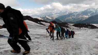 Gezginler dağ boyunca yükselirler buz yamacından geçerler. Şarjör. Sıradışı spor ve hobi anlayışı, dağ sırasının arka planındaki tırmanışçılar ve ağır bulutlar. 
