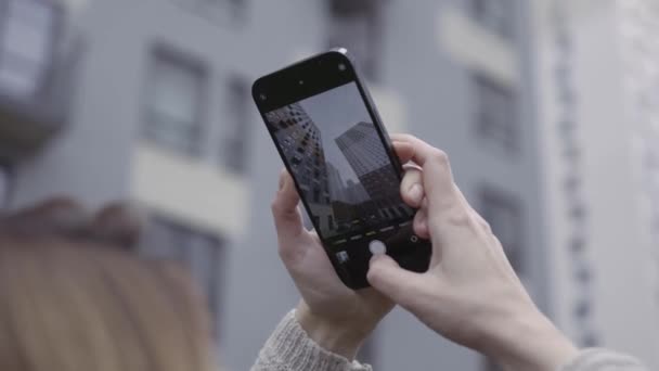 Vista sobre el hombro de las manos de las mujeres tomando fotos de un complejo residencial. Acción. Mujer usando smartphone para fotografiar edificios modernos de gran altura. — Vídeos de Stock