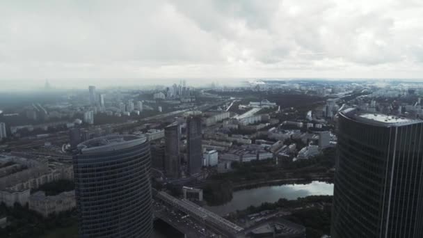 Beeindruckender Rundblick auf Wolkenkratzer moderner Architektur an einem nebligen Tag. Handeln. Luftaufnahme einer modernen Stadt mit fließendem Fluss und grüner Vegetation, die an ihren Ufern wächst. — Stockvideo
