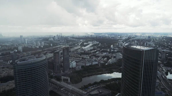 Impressionnante vue panoramique sur les tours d'architecture moderne gratte-ciel par une journée brumeuse. L'action. Vue aérienne d'une ville moderne avec une rivière et une végétation verdoyante poussant le long de ses rives. — Photo