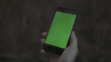 Elinde yeşil ekran olan akıllı telefonu tutan bir adama yaklaş. Hisse. Bulanık arkaplanda krom anahtarı olan modern cep telefonu.