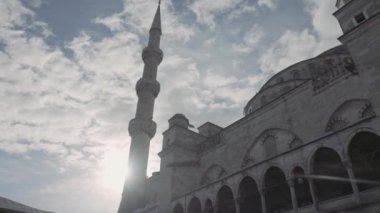 Mavi bulutlu gökyüzü ve parlayan güneşin arka planında antik ve güzel bir cami manzarası. Başla. Din ve mimari kavramı.