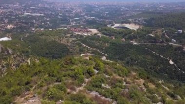 Güneşli yaz gününün ve yeşil dağ yamacının havadan görünüşü. Şarjör. Güzel kayaların üzerinde uçan kozalaklı ormanlarla ve vadideki bir köyle.