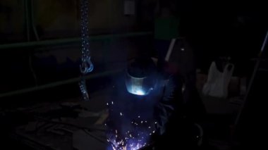 Üniformalı bir işçi ve kaynak yaparken maske takan bir işçi. Şarjör. Metal detaylarıyla çalışan bir fabrikanın atölyesinde kaynakçı..