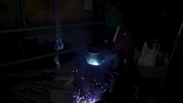 Ein mühevoller Arbeiter in Uniform und Schutzmaske während des Schweißvorgangs. Clip. Schweißer in der Werkstatt eines Werkes, das mit Metalldetails arbeitet. — Stockvideo