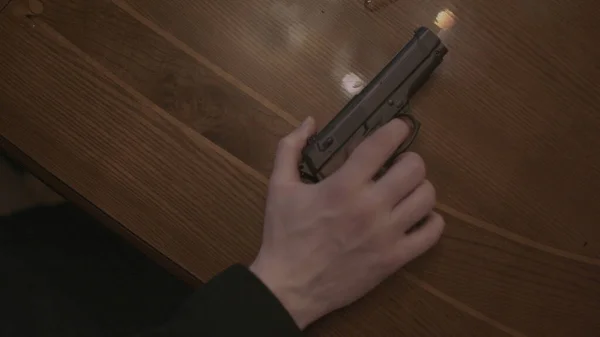 Caucasian male hand placing gun on wooden table. Action. Close up top view of man putting his hand with a firearm on a brown wooden table. — Stock Photo, Image