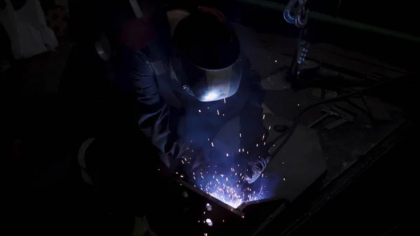 在焊接过程中穿着制服和防护面罩的勤劳的工人。剪断。车间中处理金属细节的焊机. — 图库照片