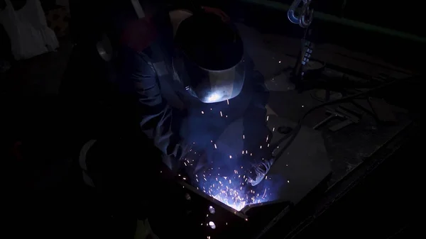 Um trabalhador laborioso em um uniforme e uma máscara de proteção durante o processo de soldagem. Clipe. Soldador em uma oficina de uma fábrica que trabalha com detalhes de metal. — Fotografia de Stock