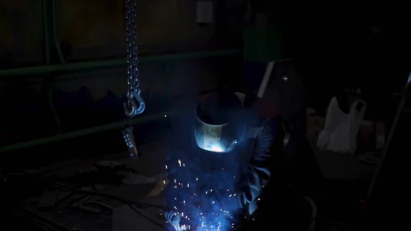 Um trabalhador laborioso em um uniforme e uma máscara de proteção durante o processo de soldagem. Clipe. Soldador em uma oficina de uma fábrica que trabalha com detalhes de metal. — Fotografia de Stock