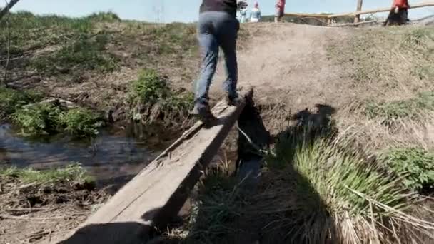 Primo piano di bambini che attraversano uno stretto ruscello su un tronco di legno. Clip. Un ragazzo che corre su una trave di legno e un altro che cammina lentamente con cautela. — Video Stock