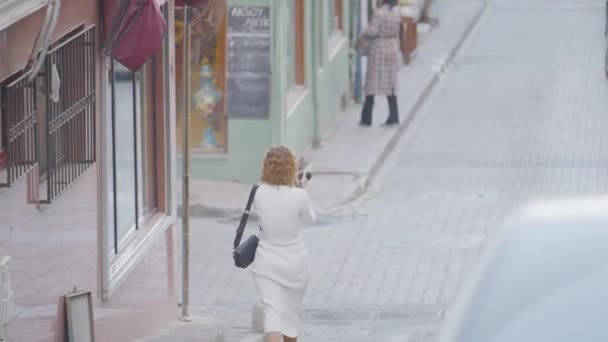 Gyönyörű nő a város utcáit fotózza. Felvétel. Vonzó nő fehér ruhában képeket készít forgalmas városról a kamera előtt. — Stock videók