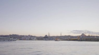 İstanbul 'a giden gemilerin zamanı. Başla. Güzel bir liman manzarası var. Geçmekte olan tekneleri ve camileri olan bir köprüsü var. Alacakaranlıkta camileri olan sahil