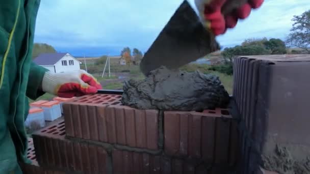 흙손과 시멘트 모르타르를 사용하는 건설 노동자. 클립. 제복을 입고 장갑을 끼고 벽돌공을 덮어 붉은 벽돌 벽을 만든다. — 비디오