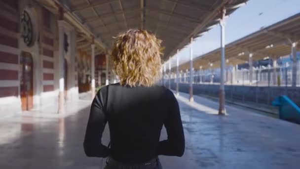 Schöne Frau, die durch den Bahnhof geht. Handeln. Rückansicht einer attraktiven Frau, die selbstbewusst vor dem Hintergrund des Bahnhofs geht. Schöne Frau mit kurzen Haaren spaziert an sonnigen Tagen durch die Stadt — Stockvideo