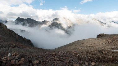 Kayalık tepelerin ve mavi gökyüzünün tepelerinde bulutlar olan kayalık dağlar. Şarjör. Dağlarda güneşli bir gün ve sabah sisi, Kuzey Şelaleleri Ulusal Parkı.